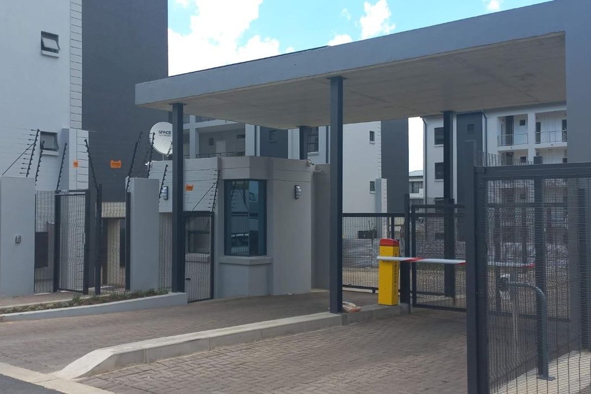 Secure apartment complex entrance featuring a guard house, boom gate access control, and perimeter electric fencing.