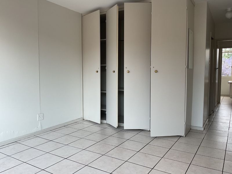 An empty bedroom featuring tiled flooring and built-in cupboards, showing signs of minor water damage on the lower wall section.