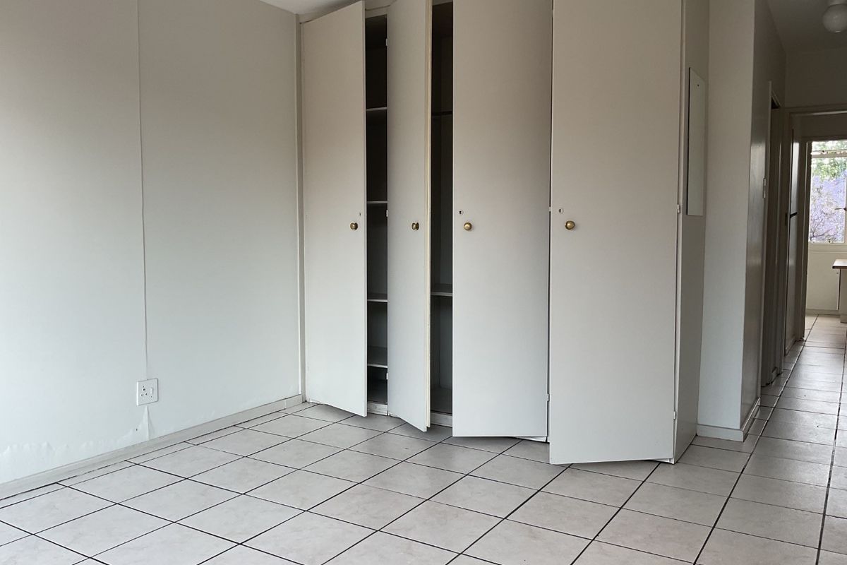 An empty bedroom featuring tiled flooring and built-in cupboards, showing signs of minor water damage on the lower wall section.