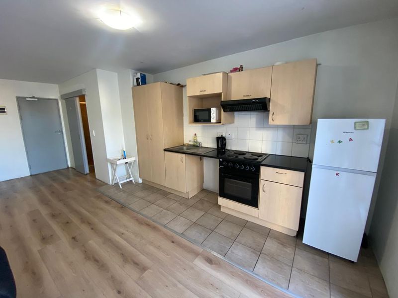 Open-plan living area featuring a functional kitchen with light wood cabinetry, built-in oven, hob, extractor fan, and durable tiled flooring.