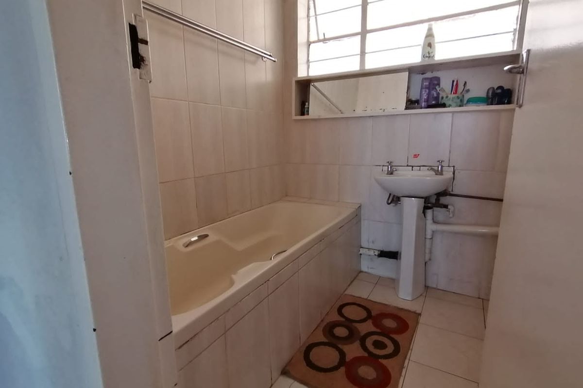 A compact bathroom featuring a built-in bathtub, pedestal basin, and tiled walls, requiring cosmetic updates to modernize the space.