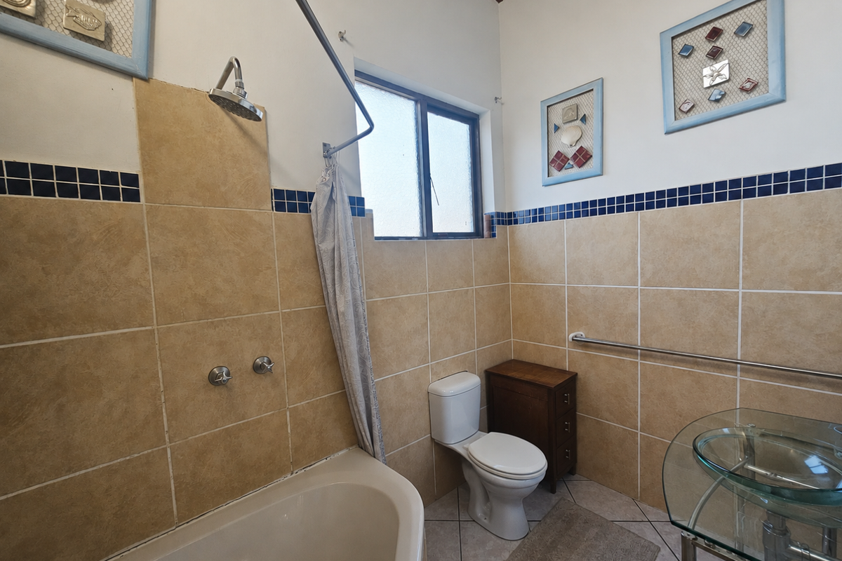 A functional bathroom featuring a combined shower and bathtub, a standard toilet, and a glass vessel sink with wall-mounted fixtures.