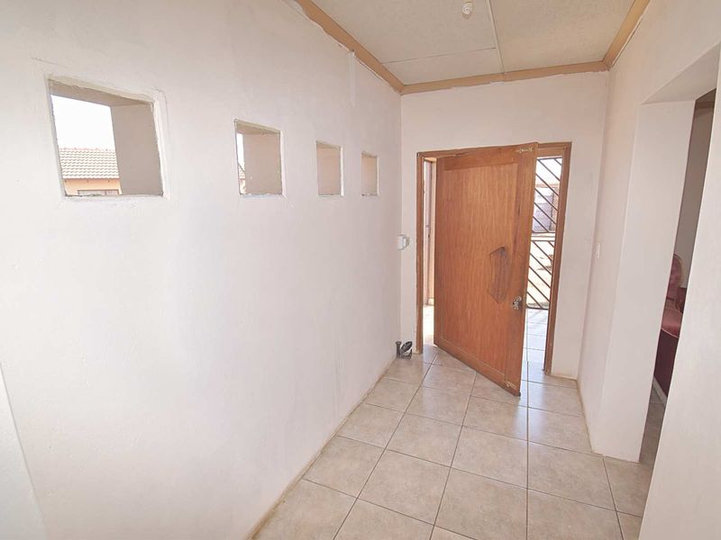 An empty entrance hall featuring tiled flooring, a wooden door with a security gate, and unique decorative wall cutouts.