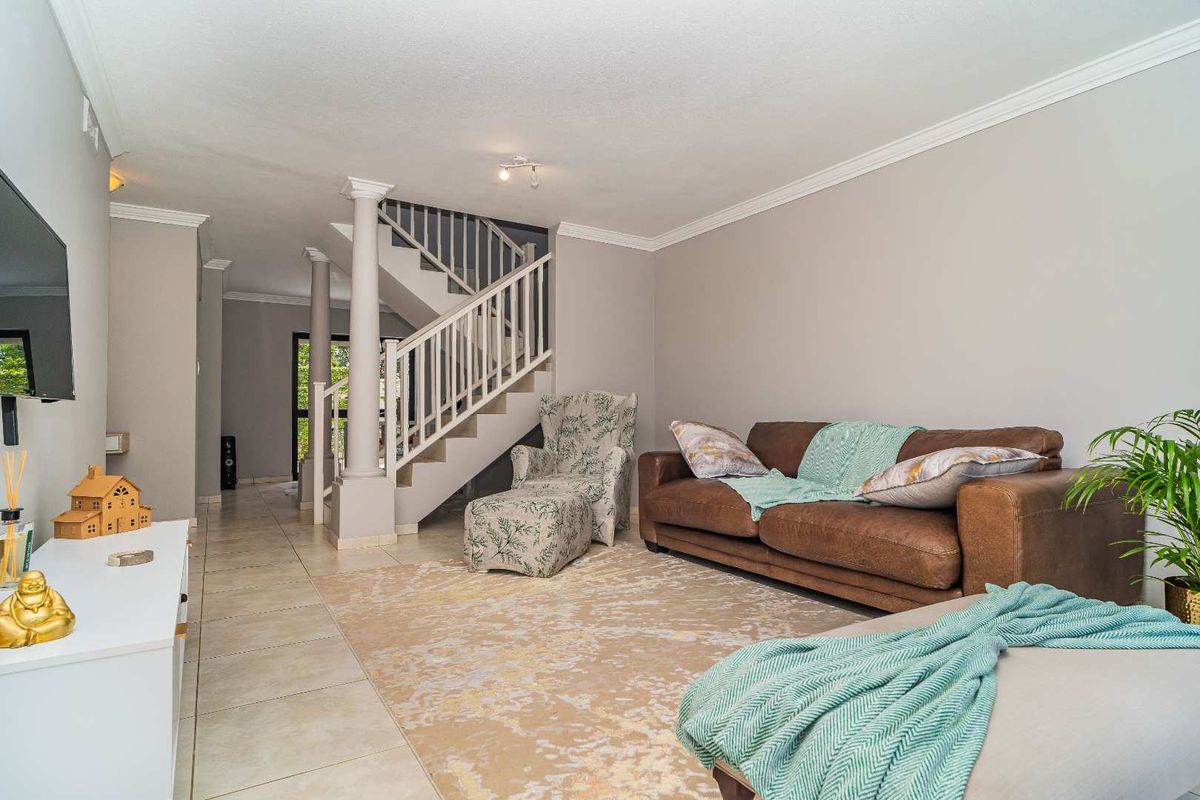 Open plan living area featuring a staircase with decorative columns and tiled flooring, leading towards the rear entrance.