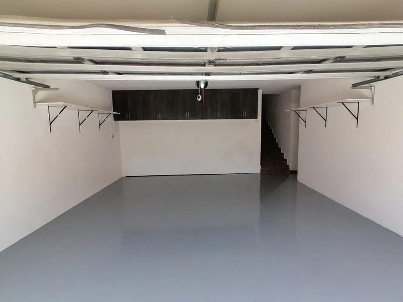 Spacious double garage featuring a clean epoxy-coated floor, overhead storage cabinets, wall-mounted shelving brackets, and direct access to an internal staircase.