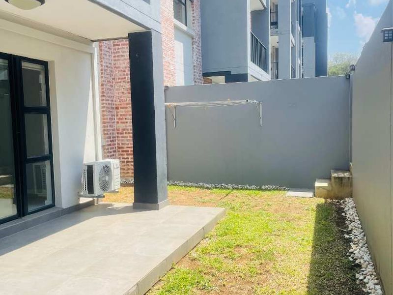 A private ground-floor apartment rear garden featuring a tiled patio, small lawn area, and boundary wall with a wall-mounted drying rack.