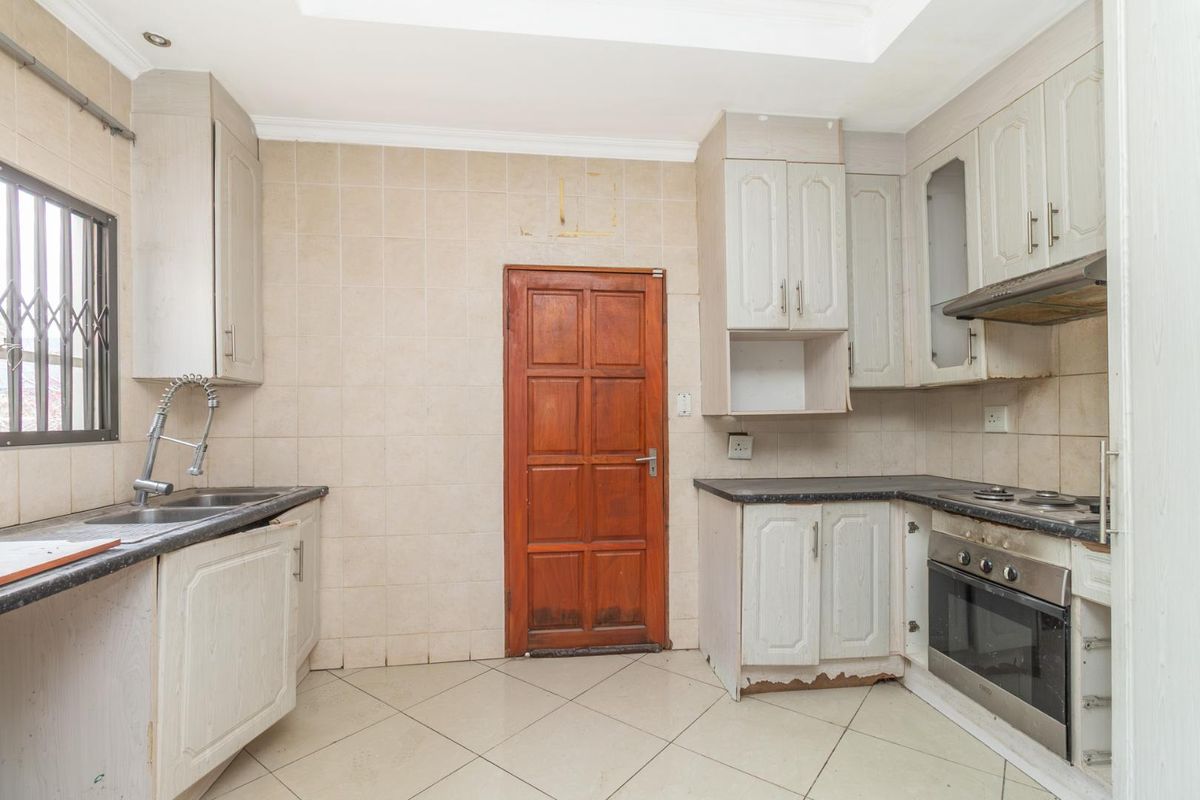 A dated kitchen featuring tiled walls, built-in cabinetry, a stainless steel oven, and a sink with a gooseneck faucet.