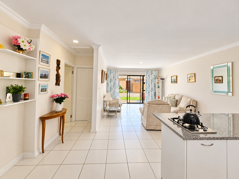 Spacious open-plan living area featuring tiled flooring, a modern kitchen island with granite countertop and gas hob, and direct access to a rear patio.