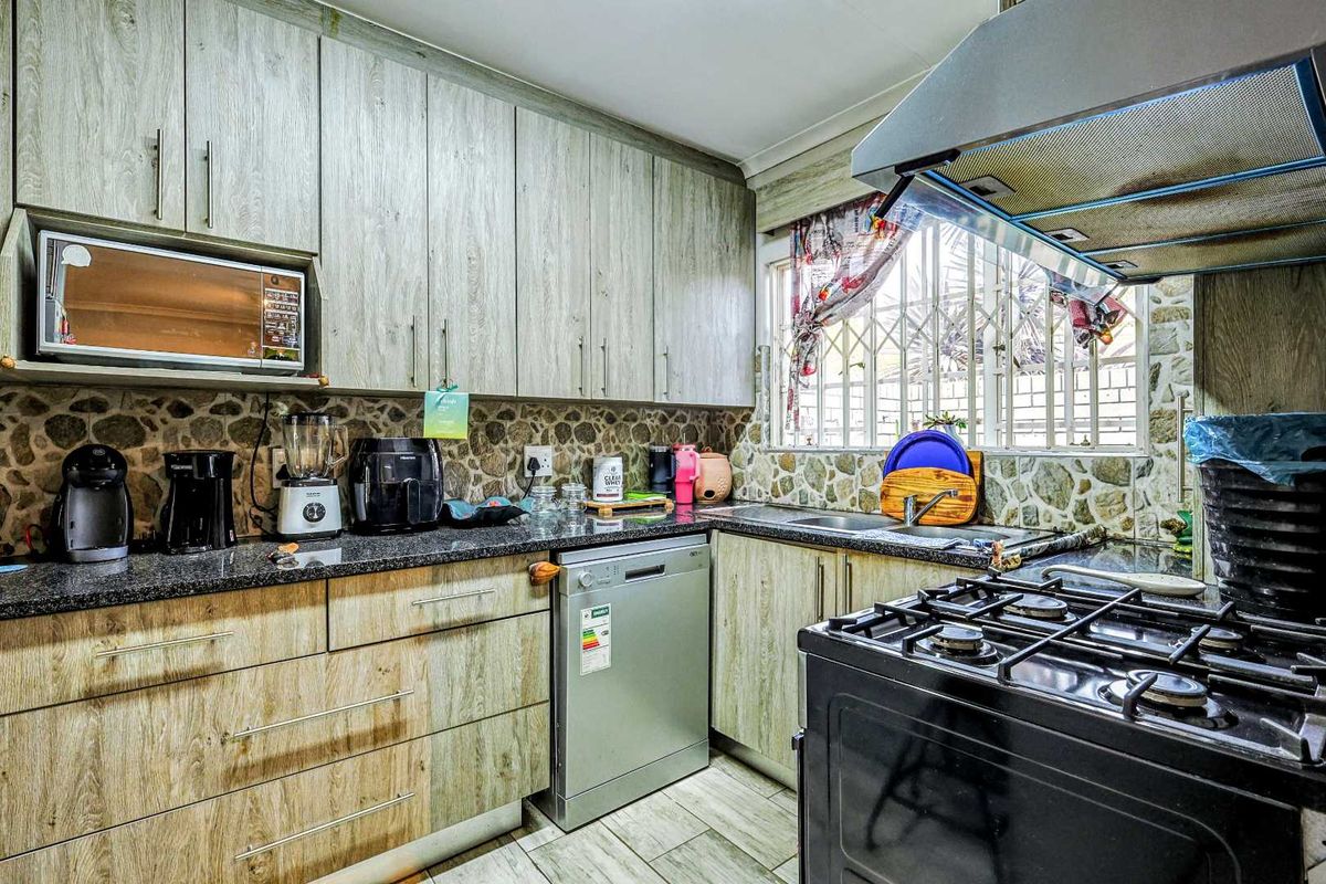 Functional kitchen featuring wood-look cabinetry, granite countertops, stone-clad backsplash, and a built-in extractor fan, offering a practical layout for daily meal preparation.