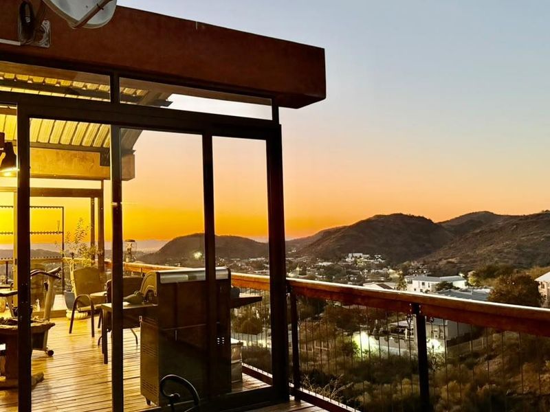 Elevated balcony featuring timber decking and expansive views of the surrounding landscape, accessible through large sliding glass doors.