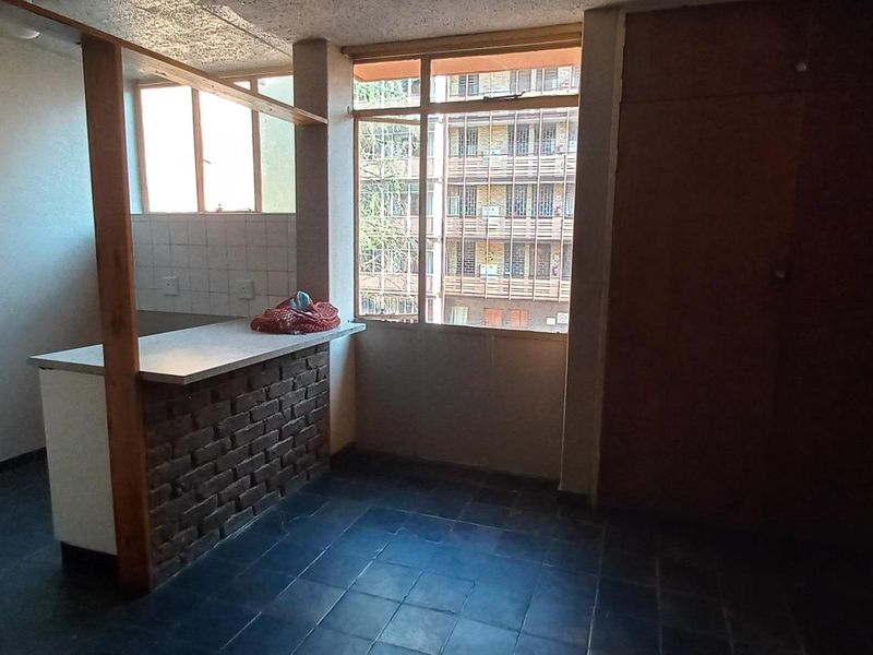 Open plan living area featuring a brick breakfast bar, built-in cupboards, and tiled flooring with large windows providing natural light.