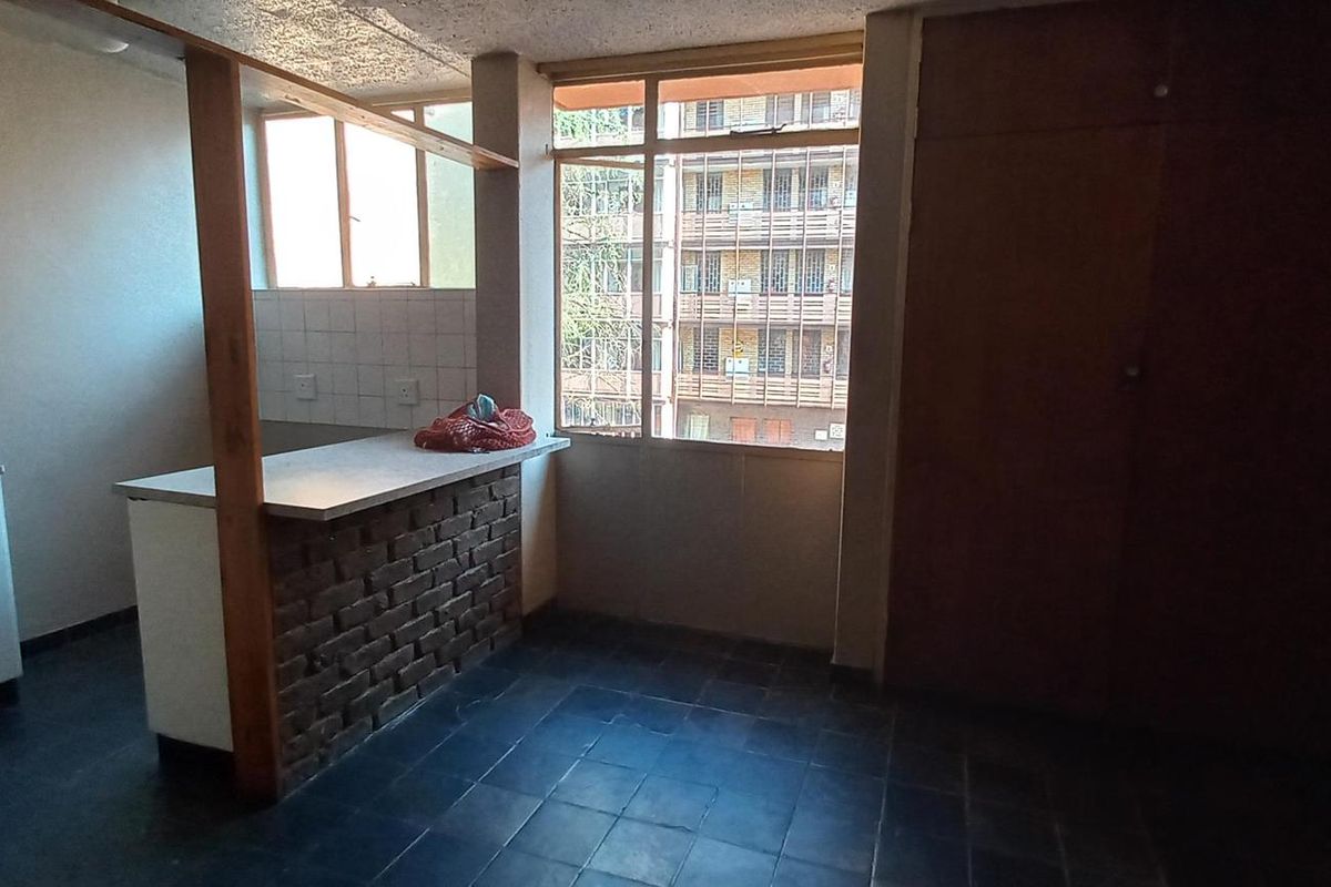 Open plan living area featuring a brick breakfast bar, built-in cupboards, and tiled flooring with large windows providing natural light.