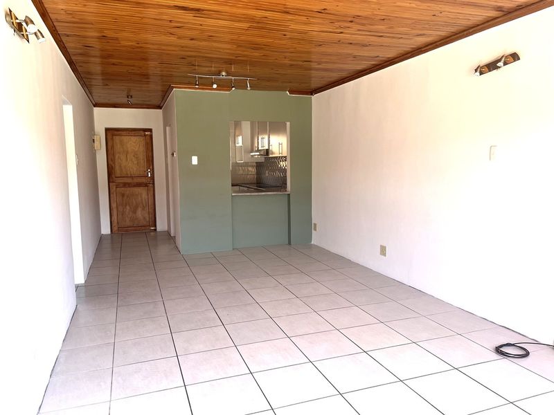 Open plan living area featuring ceramic floor tiles, a timber tongue and groove ceiling, and a convenient pass-through window to the kitchen.