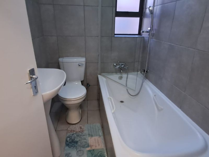 A functional bathroom featuring a pedestal basin, toilet, and a bathtub with a shower mixer, finished with neutral wall and floor tiles.
