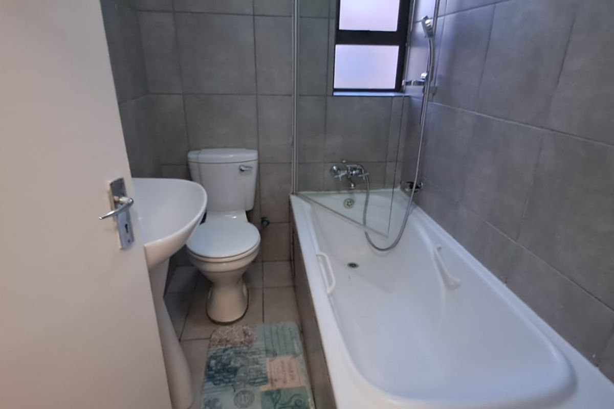 A functional bathroom featuring a pedestal basin, toilet, and a bathtub with a shower mixer, finished with neutral wall and floor tiles.