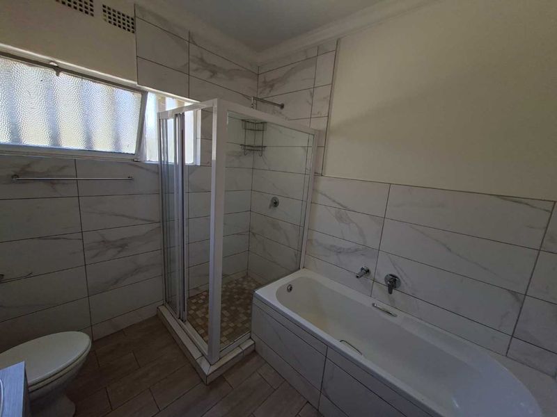 A modern bathroom featuring a glass shower enclosure, a built-in bathtub, and contemporary marble-look wall tiling with wood-effect floor tiles.