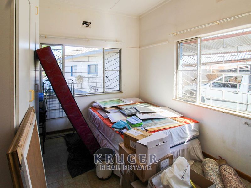 A bedroom featuring built-in cupboards, tiled flooring, and security bars on the windows, requiring some cosmetic updates to restore its appeal.