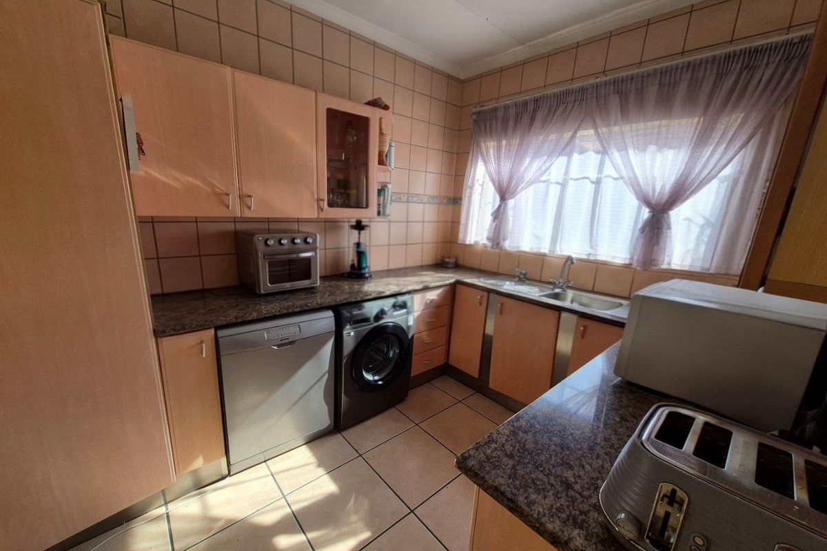 A functional kitchen featuring laminate cabinetry, granite countertops, and tiled finishes, offering a practical layout with integrated appliance spaces.