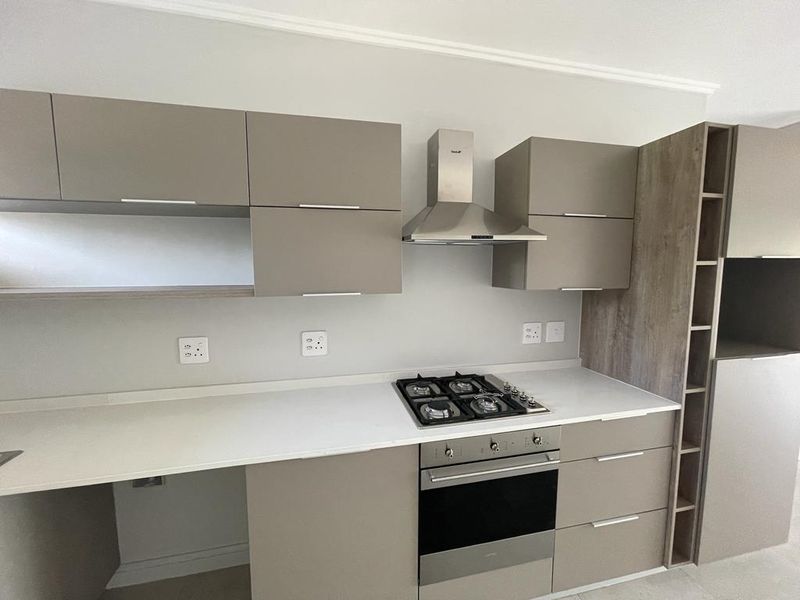 Modern kitchen featuring sleek taupe cabinetry, stone countertops, a built-in gas hob, oven, and stainless steel extractor fan.