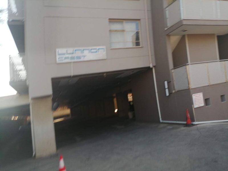 Exterior view of the Lunnon Crest apartment building entrance, featuring a covered parking access area and balcony structures.