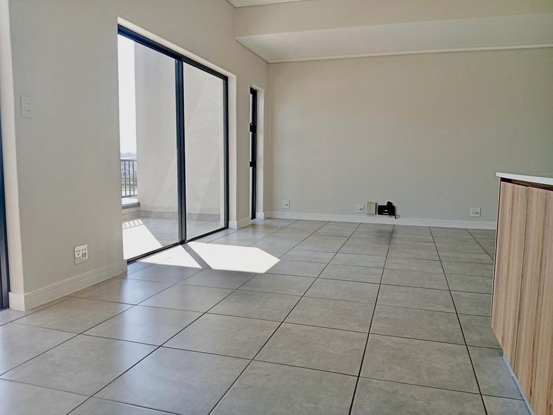A bright, empty open-plan living area featuring neutral tiled flooring, modern finishes, and a large sliding glass door leading to an outdoor balcony.
