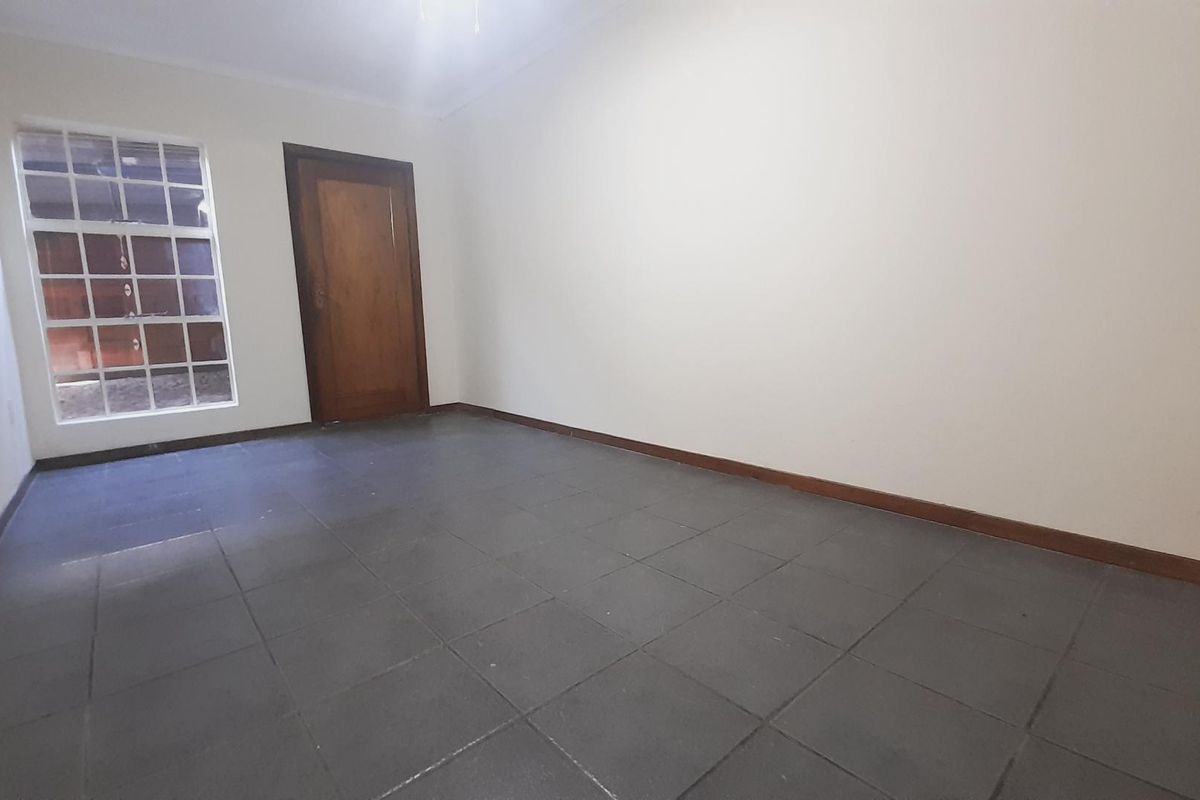 A vacant bedroom featuring tiled flooring, a wooden door, and a window with security bars.