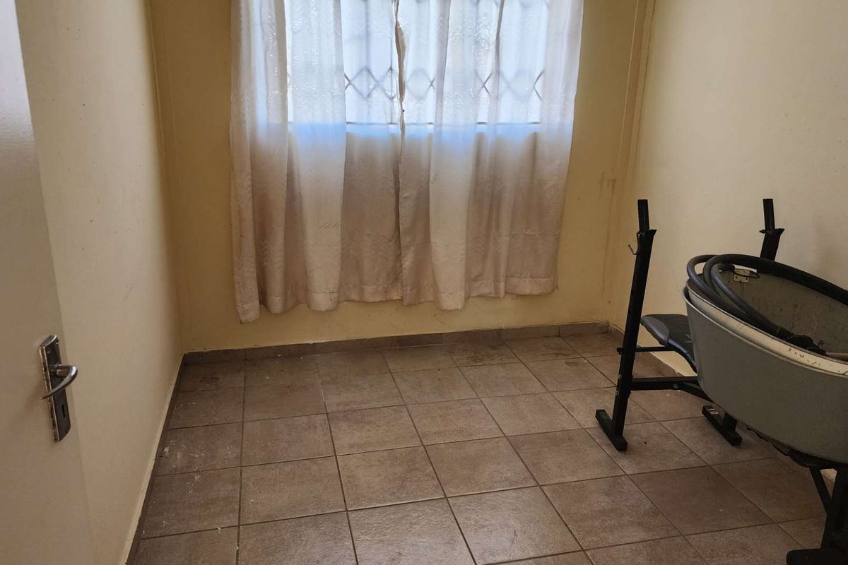 A small, functional room featuring tiled flooring and a window with security bars, suitable for use as a bedroom or home office.