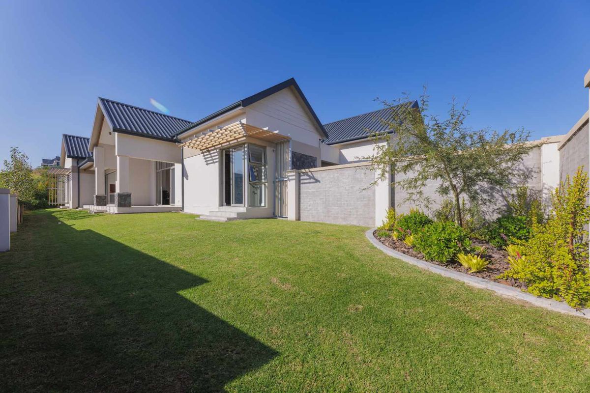 A well-maintained rear garden featuring a manicured lawn, landscaped garden beds, and a modern house exterior with a timber pergola.