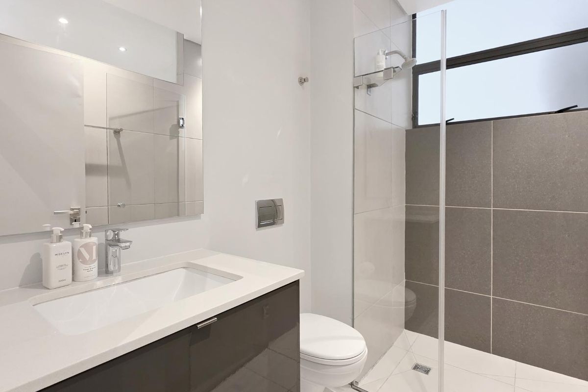 Modern bathroom featuring a sleek vanity with quartz countertop, walk-in shower with glass screen, and contemporary tiled finishes.