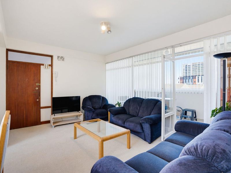 A bright living room featuring neutral carpeting, a timber entrance door, and large glass sliding doors providing access to an adjoining balcony.