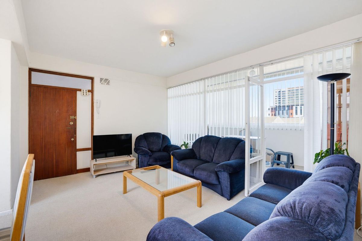 A bright living room featuring neutral carpeting, a timber entrance door, and large glass sliding doors providing access to an adjoining balcony.