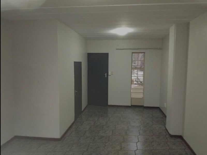 An empty, neutrally painted living area featuring tiled flooring, a ceiling light, and access to an adjacent space via an internal door.