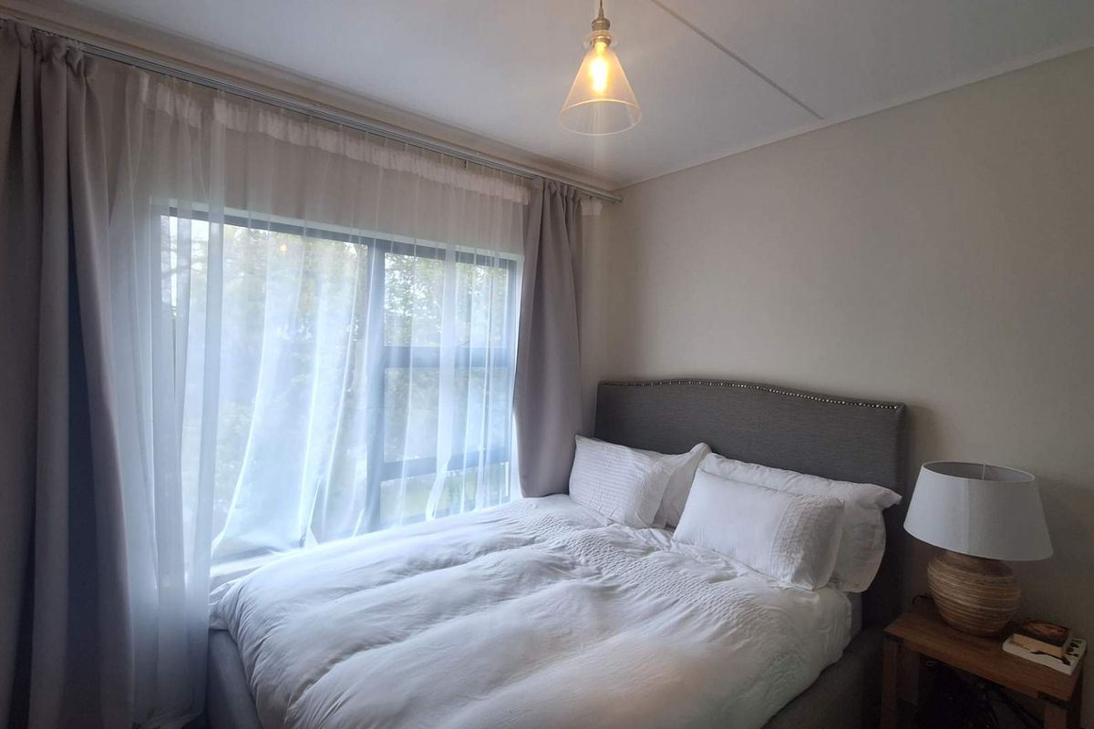 A cozy bedroom featuring a large window that allows for natural light, complemented by a simple pendant light fixture.