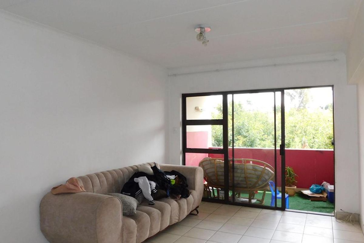 A living room featuring tiled flooring and a large sliding glass door that provides access to an outdoor balcony area.