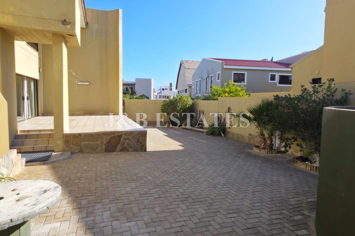 A paved rear courtyard area featuring a raised patio section, perimeter boundary walls, and direct access to the main dwelling.