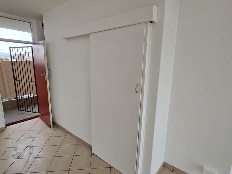 An empty entry area featuring tiled flooring, a white sliding door, and a security gate leading to an outdoor balcony space.