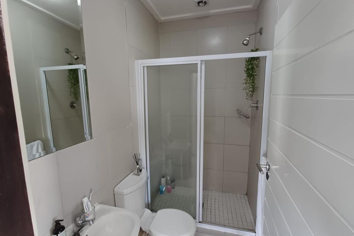 A functional bathroom featuring a glass-enclosed shower, a wall-mounted mirror, a pedestal basin, and a standard toilet with neutral wall tiling.