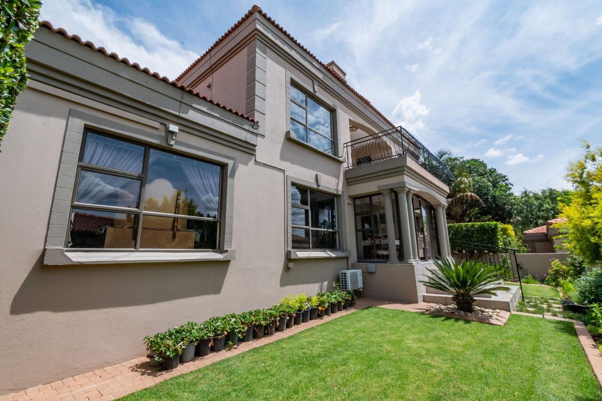Rear view of the townhouse featuring a landscaped garden, paved walkway, balcony with wrought iron railing, and classic architectural detailing.