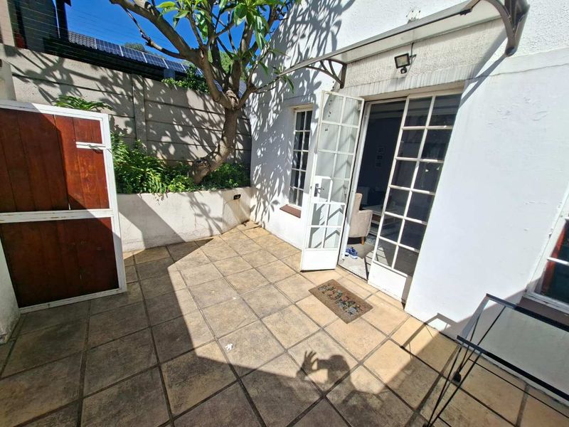 A private paved patio area featuring a retaining wall, mature tree, and direct access to the interior through classic French doors.
