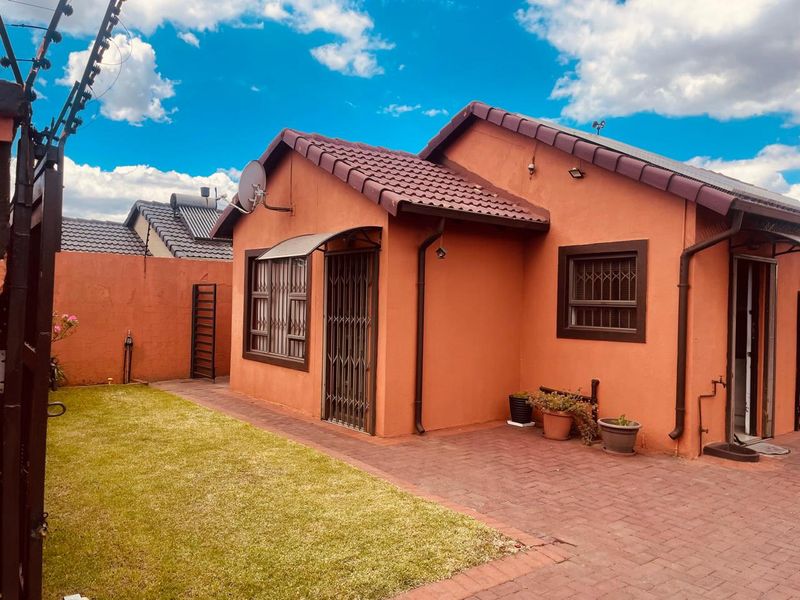 Rear view of the house featuring a paved patio area, small lawn, security gates, and electric fencing.