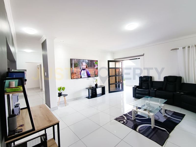 A bright and spacious living room featuring polished tiled flooring, recessed ceiling lights, and direct access to the outdoor area through a glass panel door.