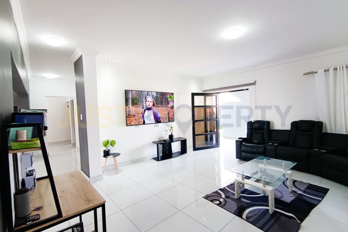 A bright and spacious living room featuring polished tiled flooring, recessed ceiling lights, and direct access to the outdoor area through a glass panel door.