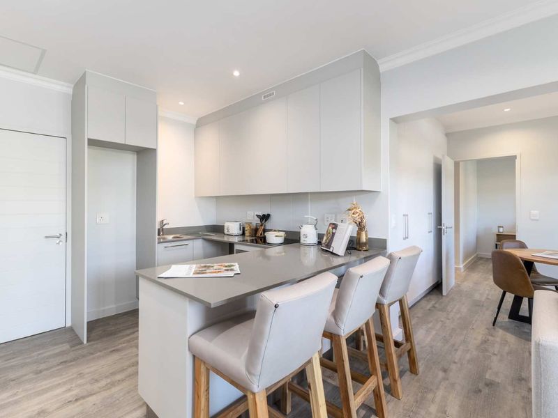 Modern open-plan kitchen featuring sleek cabinetry, stone countertops, and a breakfast bar, seamlessly flowing into the dining area with light laminate flooring.