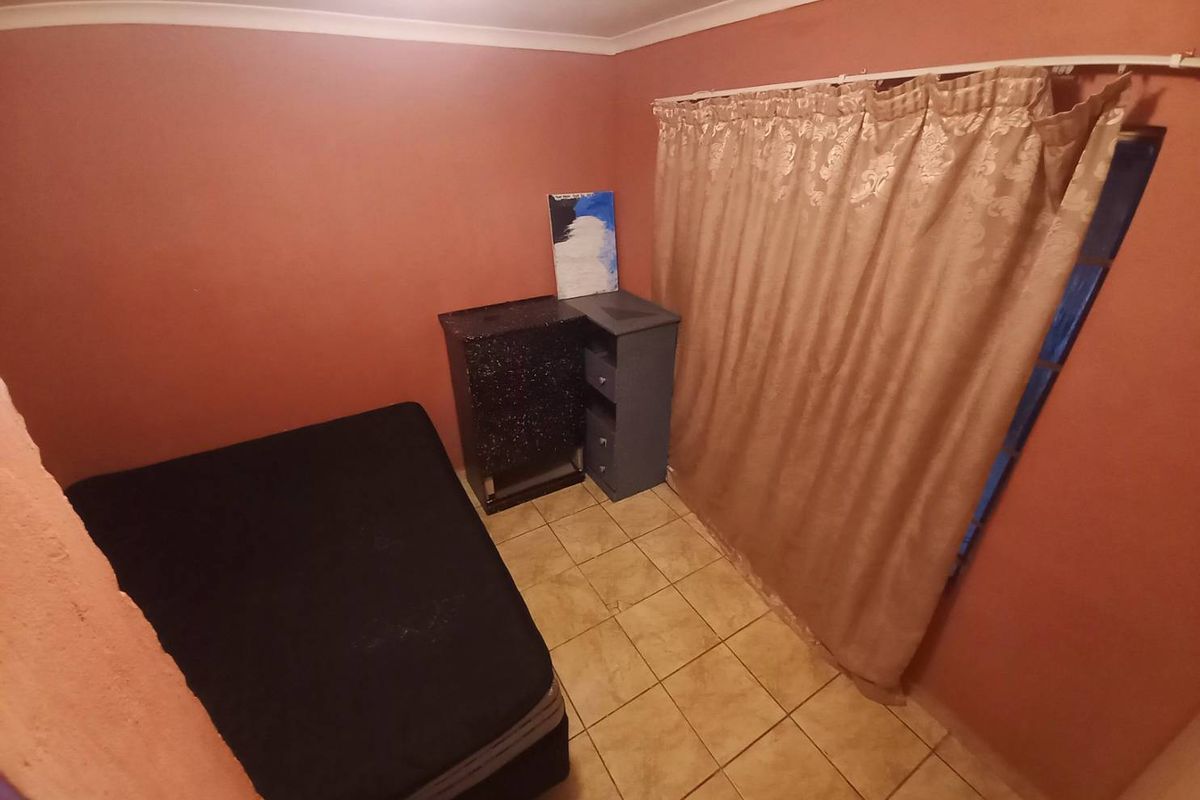 A compact bedroom featuring tiled flooring and a window covered by curtains, offering a simple and functional living space.