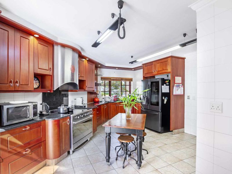 A functional kitchen featuring warm-toned wooden cabinetry, granite countertops, a stainless steel extractor fan, and a freestanding gas stove with tiled flooring.