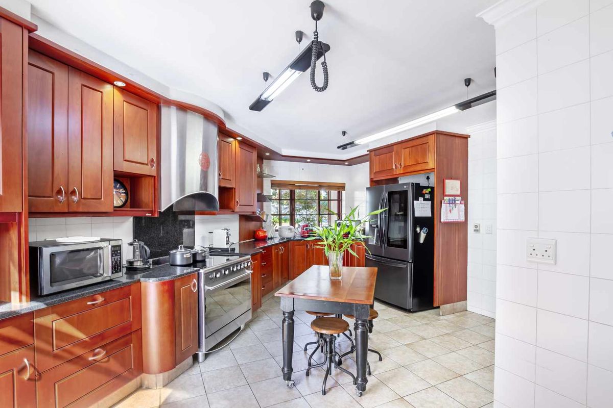 A functional kitchen featuring warm-toned wooden cabinetry, granite countertops, a stainless steel extractor fan, and a freestanding gas stove with tiled flooring.