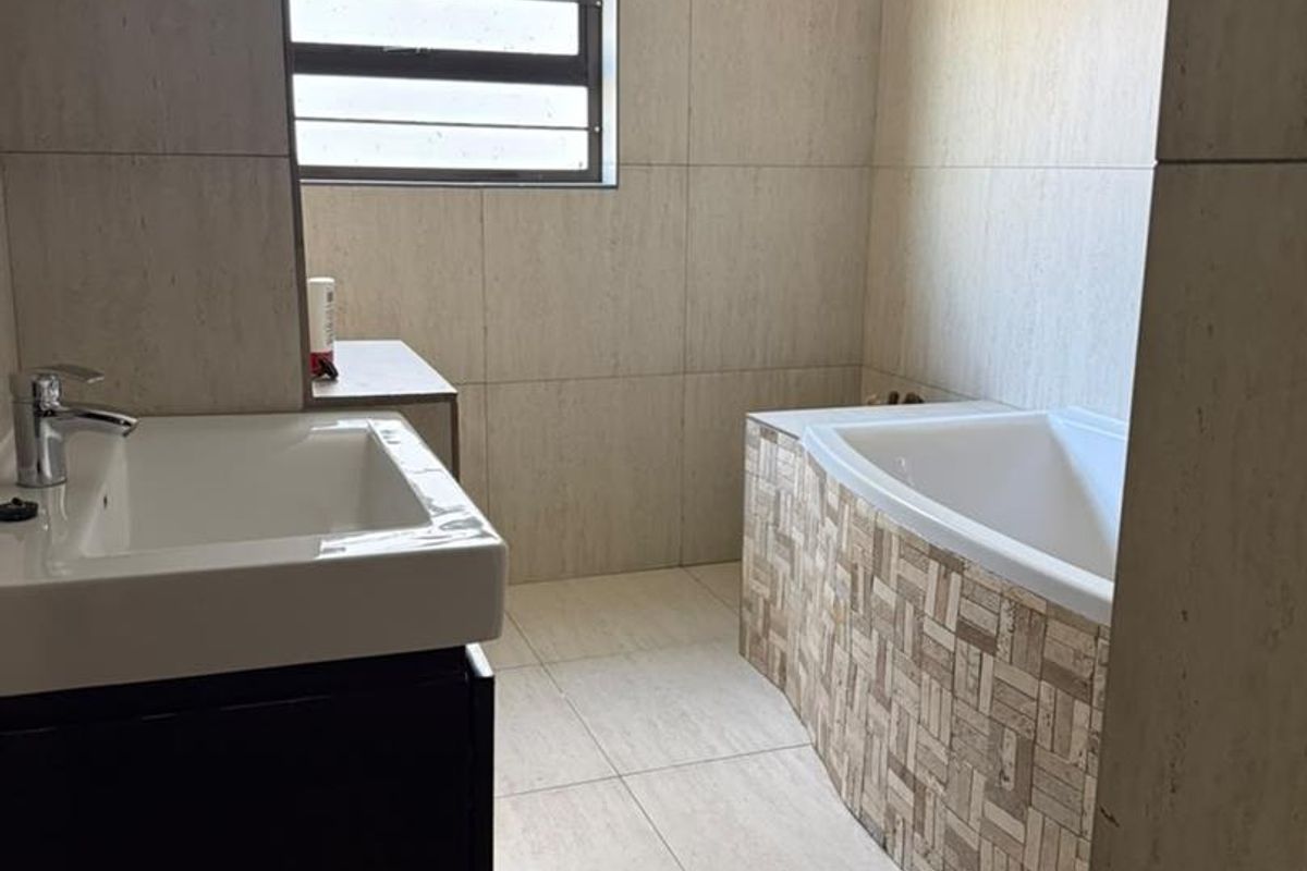 A clean, modern bathroom featuring a vanity basin, a bathtub with decorative tiling, and neutral wall and floor tiles.
