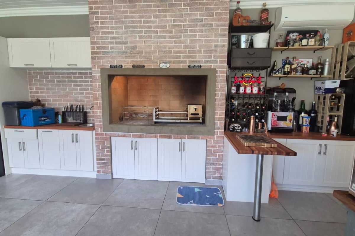 An indoor entertainment area featuring a built-in brick braai, white cabinetry, wooden countertops, and tiled flooring, creating a functional space for social gatherings.