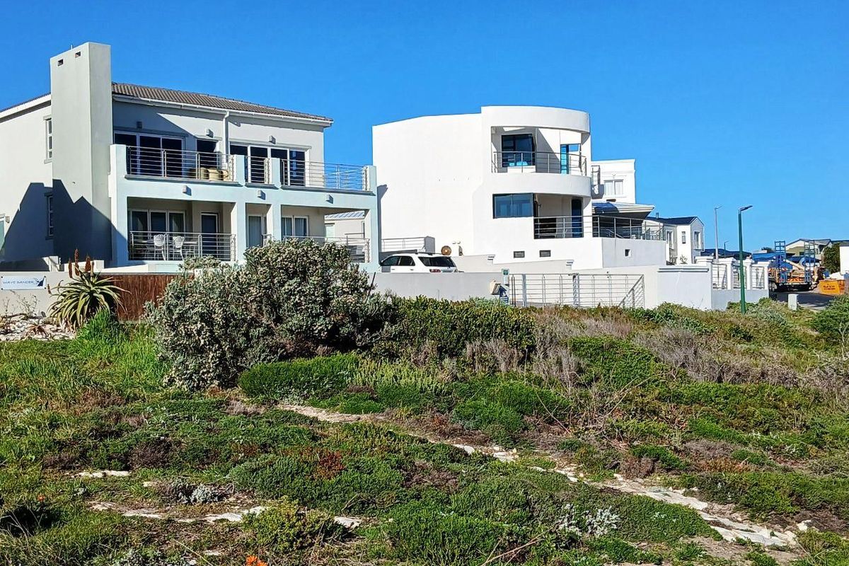 Rear view of multi-story residential properties featuring balconies, metal railings, and boundary walls, overlooking a natural coastal landscape.