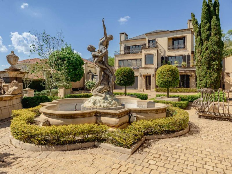 Grand multi-story residence featuring a prominent stone fountain, manicured hedges, and elegant architectural detailing in a well-maintained front garden setting.
